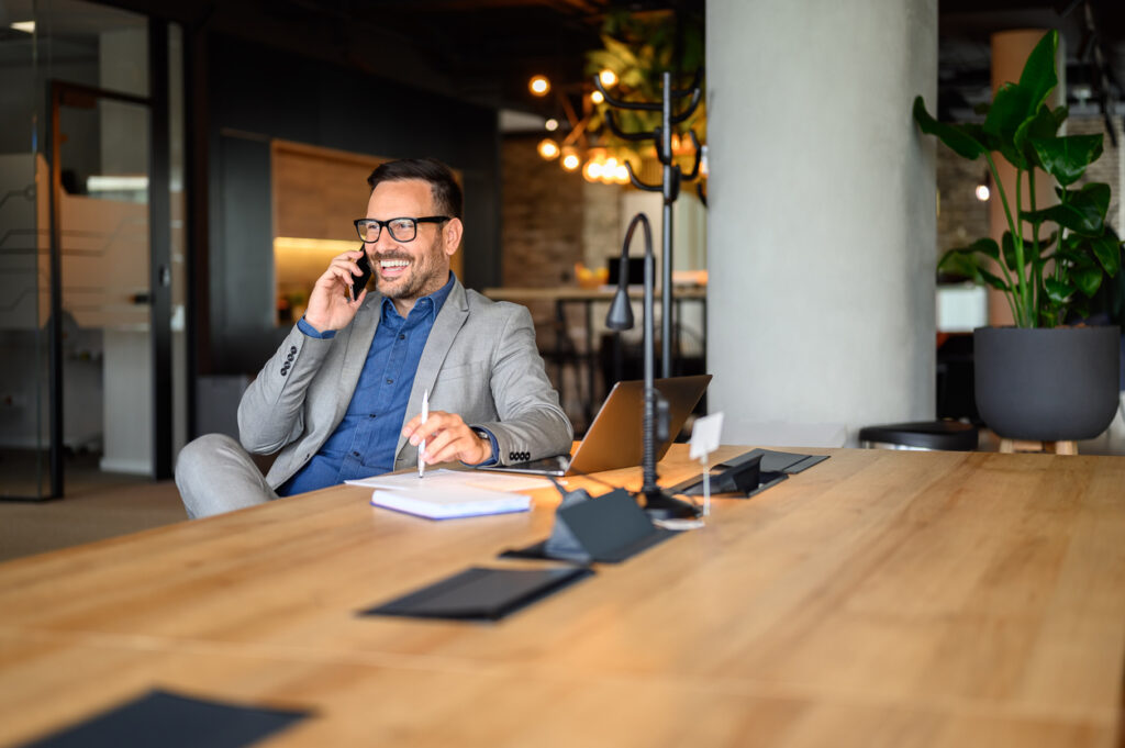 Handsome entrepreneur discussing over mobile phone while working on project at desk in modern office