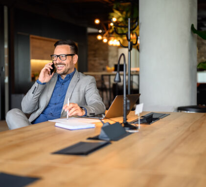Handsome entrepreneur discussing over mobile phone while working on project at desk in modern office