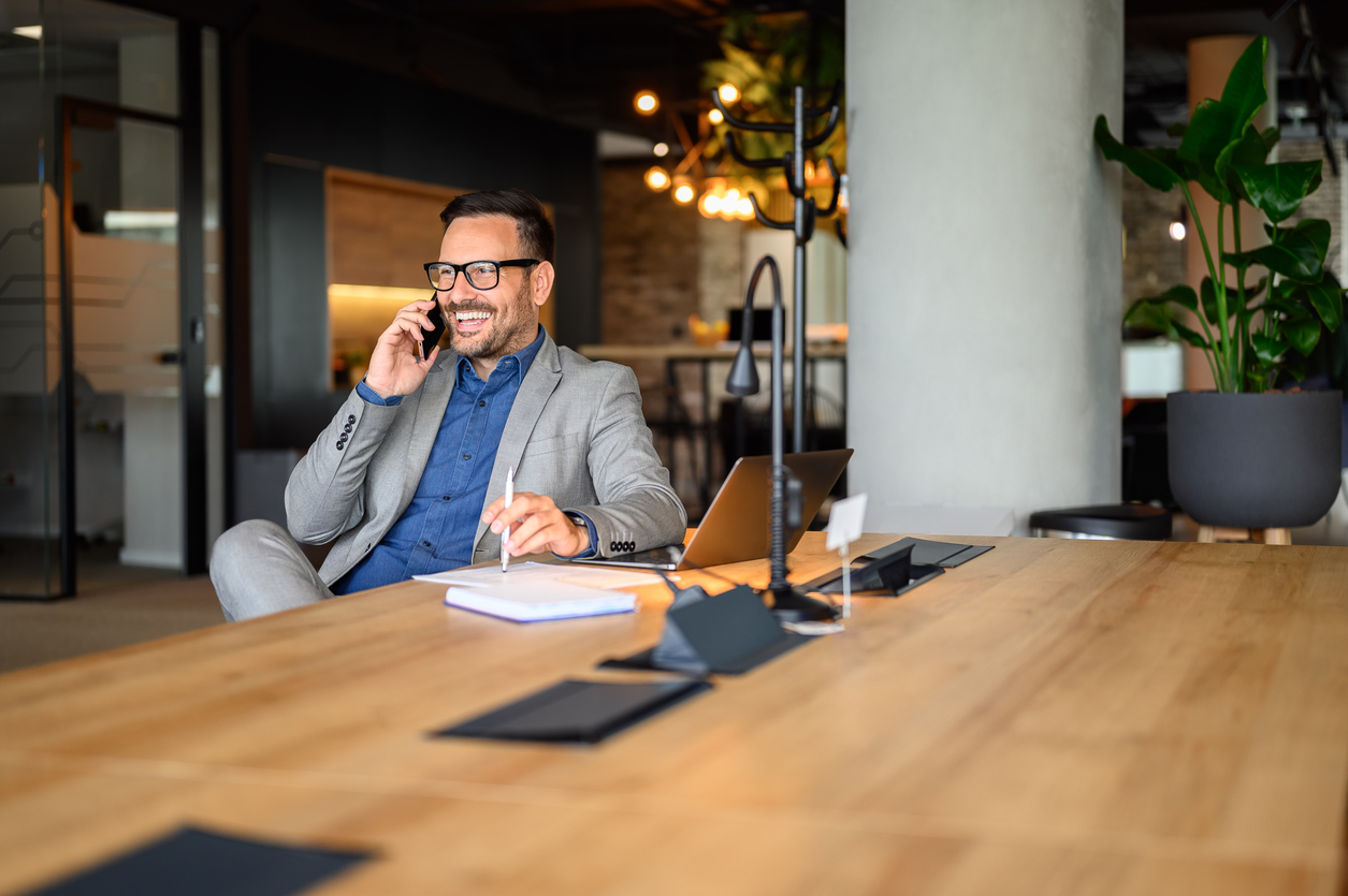 Handsome entrepreneur discussing over mobile phone while working on project at desk in modern office