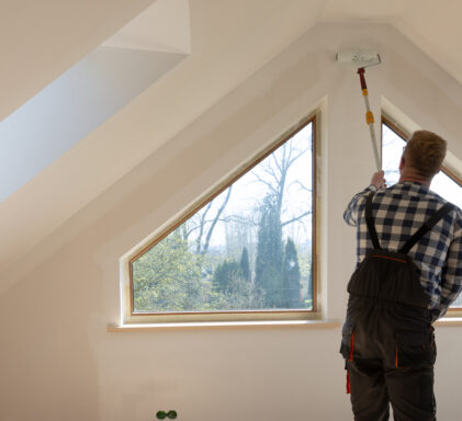 Home improvement concept, handyman painting a wall with a white paint near roof window in attic